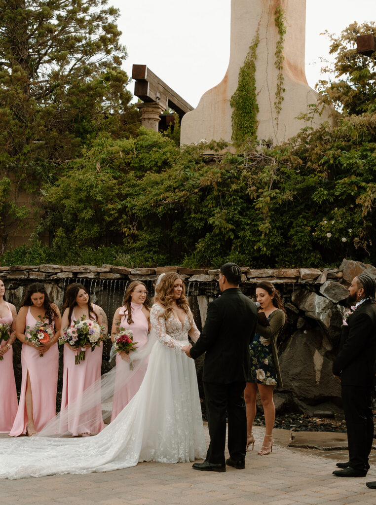 Couple exchanging rings by the fountain with their people watching